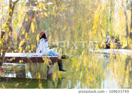 Autumn lake woman. She sits by a pond on a wooden pier in autumn and admires nature. The concept of tourism, weekends outside the city. 109633749