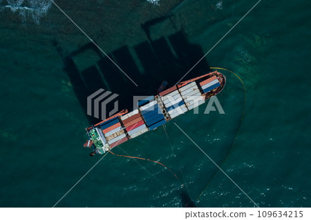 Aerial top down view of a container cargo ship stands aground after a storm with floating boom around the ship to prevent the spread of petroleum. Aerial top down view of a container cargo ship stands aground after a storm with floating boom around the ship to prevent the spread of petroleum. 109634215