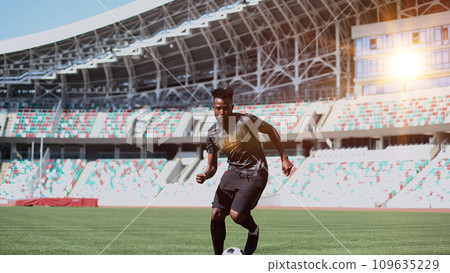 African American man playing football on the stadium field. A man runs with a soccer ball across the field. African American man playing football on the stadium field. A man runs with a soccer ball across the field. 109635229
