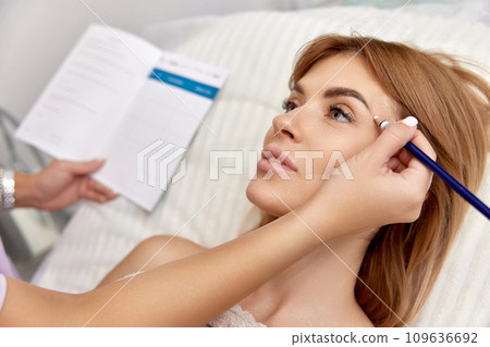 cosmetologist marking skin of caucasian woman with white pencil. facial marking for aesthetic procedure. 109636692