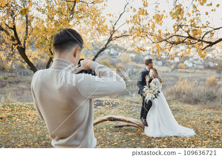 Professional wedding photographer taking pictures of the bride and groom in nature in autumn Professional wedding photographer taking pictures of the bride and groom in nature in autumn 109636721