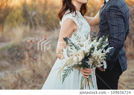 bride and groom holding beautiful bouquet in nature in autumn 109636724