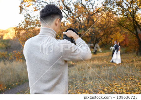Professional wedding photographer taking pictures of the bride and groom in nature in autumn 109636725