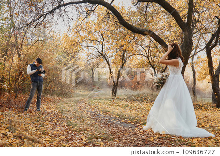 Professional wedding photographer taking pictures of the bride and groom in nature in autumn 109636727