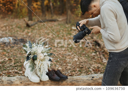 wedding photographer taking pictures of bride and groom shoes, wedding bouquet outdoor. wedding photographer taking pictures of bride and groom shoes, wedding bouquet outdoor. 109636730
