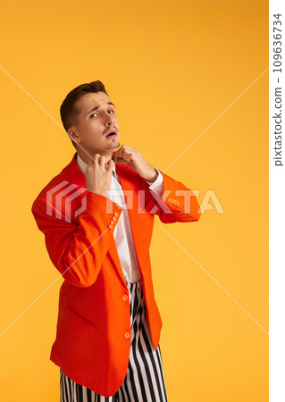 Cheerful funny young man in orange jacket and striped pants on yellow background. Cheerful funny young man in orange jacket and striped pants on yellow background. 109636734
