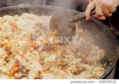 Street food festival cooks traditional Uzbek pilaf in cauldron Street food festival cooks traditional Uzbek pilaf in cauldron 109638528