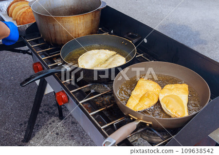 Frying pan with oil fried chebureki with street food traditional Crimean Tatar food cuisine Frying pan with oil fried chebureki with street food traditional Crimean Tatar food cuisine 109638542