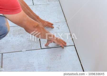 Tiler placing ceramic floor tile in position over adhesive on bathroom 109638645