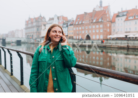 Young happy redhead woman making phone call over mobile phone in the city. Middle age woman talking on smartphone on urban background. Traveling Europe in autumn Young happy redhead woman making phone call over mobile phone in the city. Middle age woman talking on smartphone on urban background. Traveling Europe in autumn 109641051