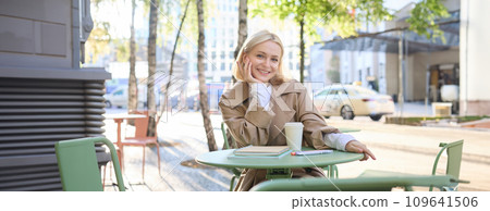 Portrait of young female student, woman with notebook, sitting in cafe and drinking coffee, smiling happily Portrait of young female student, woman with notebook, sitting in cafe and drinking coffee, smiling happily 109641506