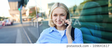 Close up portrait of smiling blond woman, chatting on the phone, talking on mobile telephone, standing on street outdoors 109641617