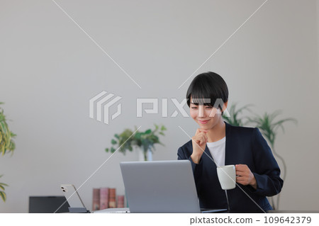 拿著咖啡杯，微笑地看著電腦螢幕 1 的女商人 109642379