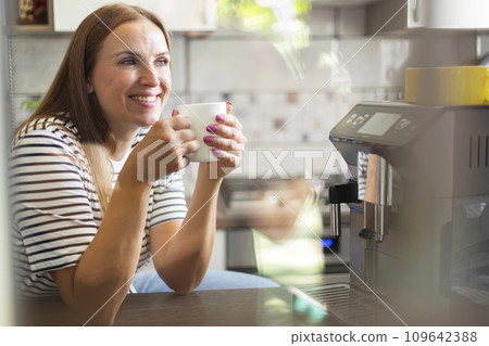 Woman enjoying freshly prepared coffee near modern coffee machine in kitchen Woman enjoying freshly prepared coffee near modern coffee machine in kitchen 109642388