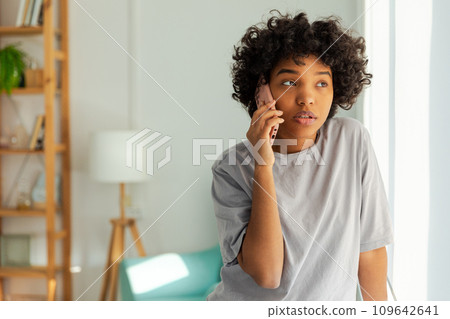 African american girl talking on smartphone at home indoor. Young woman with cell phone chatting with friends. Smiling teen girl making answering call by cellphone. Lady having conversation by mobile African american girl talking on smartphone at home indoor. Young woman with cell phone chatting with friends. Smiling teen girl making answering call by cellphone. Lady having conversation by mobile 109642641