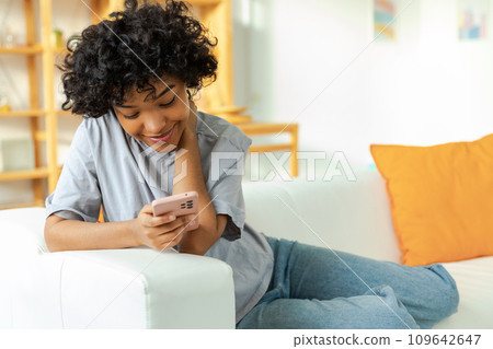African girl holding smartphone touch screen typing scroll page at home. Woman with cell phone surfing internet using social media apps playing game. Shopping online Internet news cellphone addiction 109642647