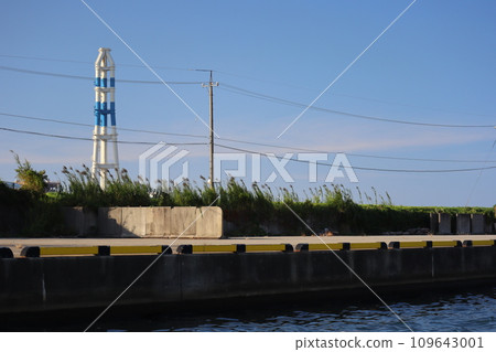 Cityscape with blue sky, clouds, chimneys, utility poles, wires, blue water canals, and riverbeds with grass. Cityscape with blue sky, clouds, chimneys, utility poles, wires, blue water canals, and riverbeds with grass. 109643001