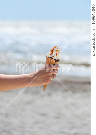 Female hand with ice cream on the background of the beach and sea. 109643040
