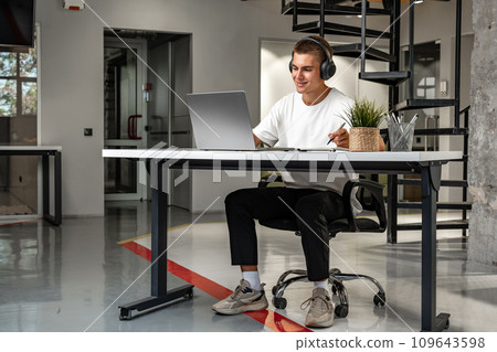 Young man wearing headphones while studying with laptop 109643598