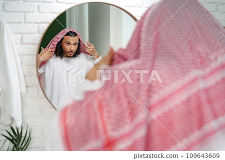 Young Arab man getting ready and looking at the mirror in the bathroom Young Arab man getting ready and looking at the mirror in the bathroom 109643609