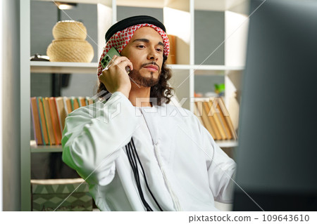 Young Arab businessman talking on the phone in the office Young Arab businessman talking on the phone in the office 109643610
