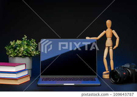 Open laptop with wooden mannequin on table against black background 109643787