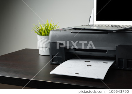 Modern printer with paper and laptop on table in office Modern printer with paper and laptop on table in office 109643790