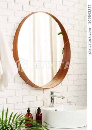 Bathroom interior with circle shaped mirror in wooden frame and white sink 109643873