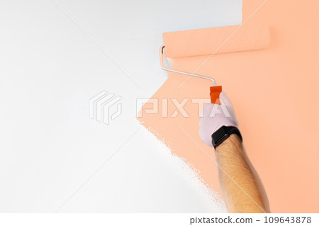 Gloved male hand painting wall into peach fuzz color of the year 2024 Gloved male hand painting wall into peach fuzz color of the year 2024 109643878