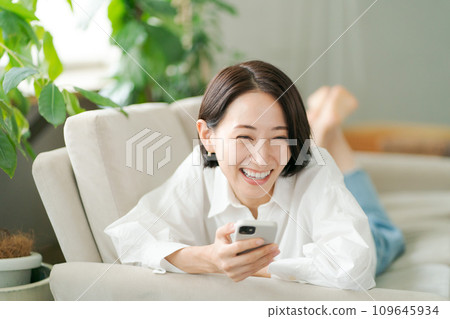 一個女人躺在沙發上，看著她的智能手機 109645934