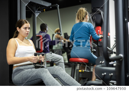 Woman is engaged in a simulator with horizontal weights in gym Woman is engaged in a simulator with horizontal weights in gym 109647930