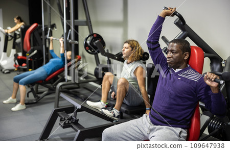 African man doing exercises on shoulder press machine in gym African man doing exercises on shoulder press machine in gym 109647938