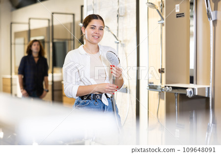 in plumbing department,woman examines shower head and quality of metal coating. 109648091