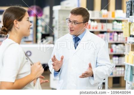 Young female and middle-aged male pharmacists talking to each-other in chemist's shop Young female and middle-aged male pharmacists talking to each-other in chemist's shop 109648094