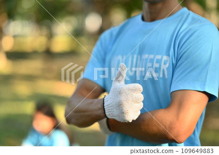 Male activist in volunteer t-shirt showing thumbs up standing outdoor 109649883