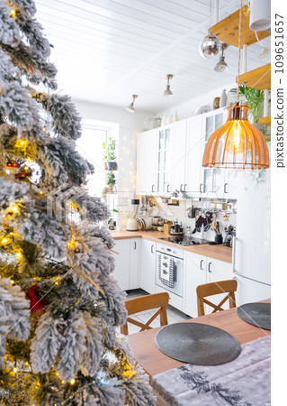 Festive Christmas decor in white kitchen, modern rustic interior with a snowy Christmas tree and fairy lights. New Year, Christmas mood, cozy home. The general plan 109651657