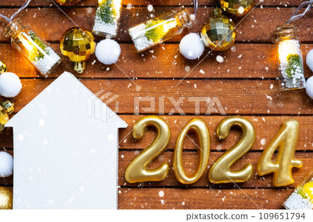 House key with tiny figure of home mock up on festive brown wooden background, lights of garlands. New Year 2024 wooden letters, greeting card. Purchase, construction, relocation, mortgage, insurance 109651794