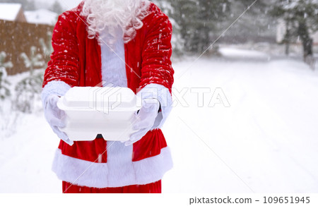 Food delivery service containers in hands of Santa Claus outdoor in snow. Christmas eve promotion. Ready-made hot order, disposable plastic box. New year holidays catering. Copy space, mock up Food delivery service containers in hands of Santa Claus outdoor in snow. Christmas eve promotion. Ready-made hot order, disposable plastic box. New year holidays catering. Copy space, mock up 109651945
