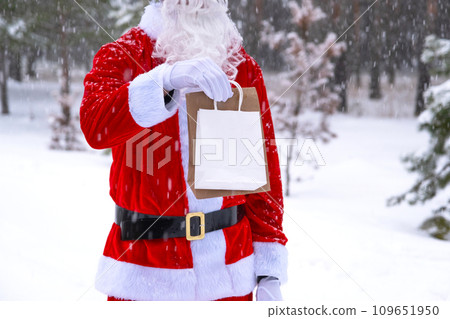 Santa Claus outdoor in winter and snow handing in hand eco paper bags with craft gift, food delivery. Shopping, packaging recycling, handmade, delivery for Christmas and New year 109651950