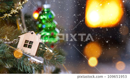 Key to the house with a keychain is hanging on the Christmas tree. A gift for New Year, Christmas. Building, design, project, moving to new house, mortgage, rent and purchase real estate. Copy space 109651953