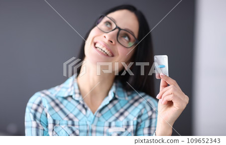 Contented woman holding blister with one capsule in her hands Contented woman holding blister with one capsule in her hands 109652343