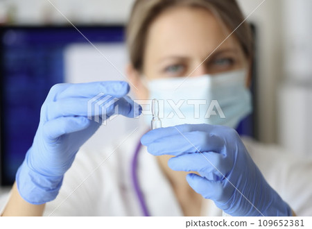 Nurse in mask and gloves holding ampoule of medicine closeup 109652381