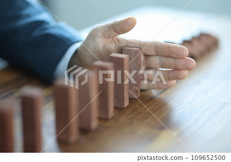 Male hand stopping falling of wooden blocks in line closeup 109652500