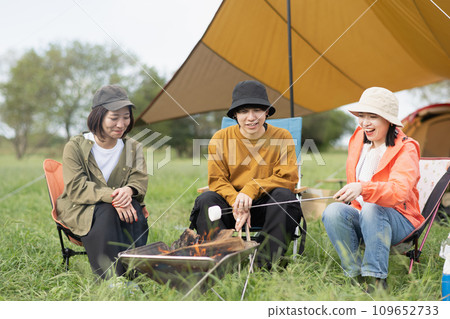 Outdoor image of young men and women enjoying camping, bonfire, and roasting marshmallows 109652733