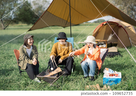 Outdoor image of young men and women enjoying camping, bonfire, and roasting marshmallows Outdoor image of young men and women enjoying camping, bonfire, and roasting marshmallows 109652735