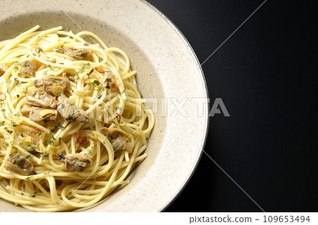 黑色背景下的 Vongole Bianco 的俯視照片，裡面有大量蛤蜊、紅辣椒、意大利歐芹和大蒜片。 109653494