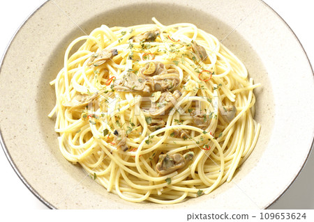 An overhead shot of Vongole Bianco with lots of clams, red chili peppers, Italian parsley, and garlic chips against a white background. An overhead shot of Vongole Bianco with lots of clams, red chili peppers, Italian parsley, and garlic chips against a white background. 109653624