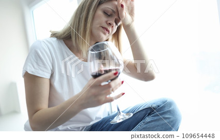 Tired woman with glass of red wine holding her head Tired woman with glass of red wine holding her head 109654448