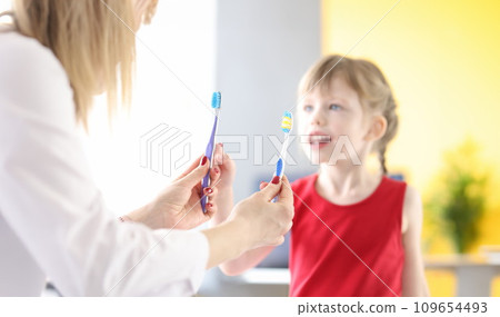 Doctor holding two toothbrushes in front of little girl Doctor holding two toothbrushes in front of little girl 109654493