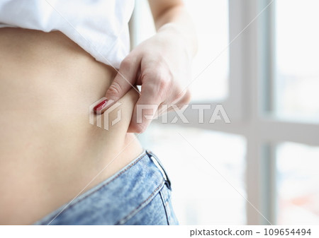 Woman pulling off fold of fat at her waist closeup 109654494